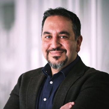 Confident man with a beard smiling warmly in a professional setting.