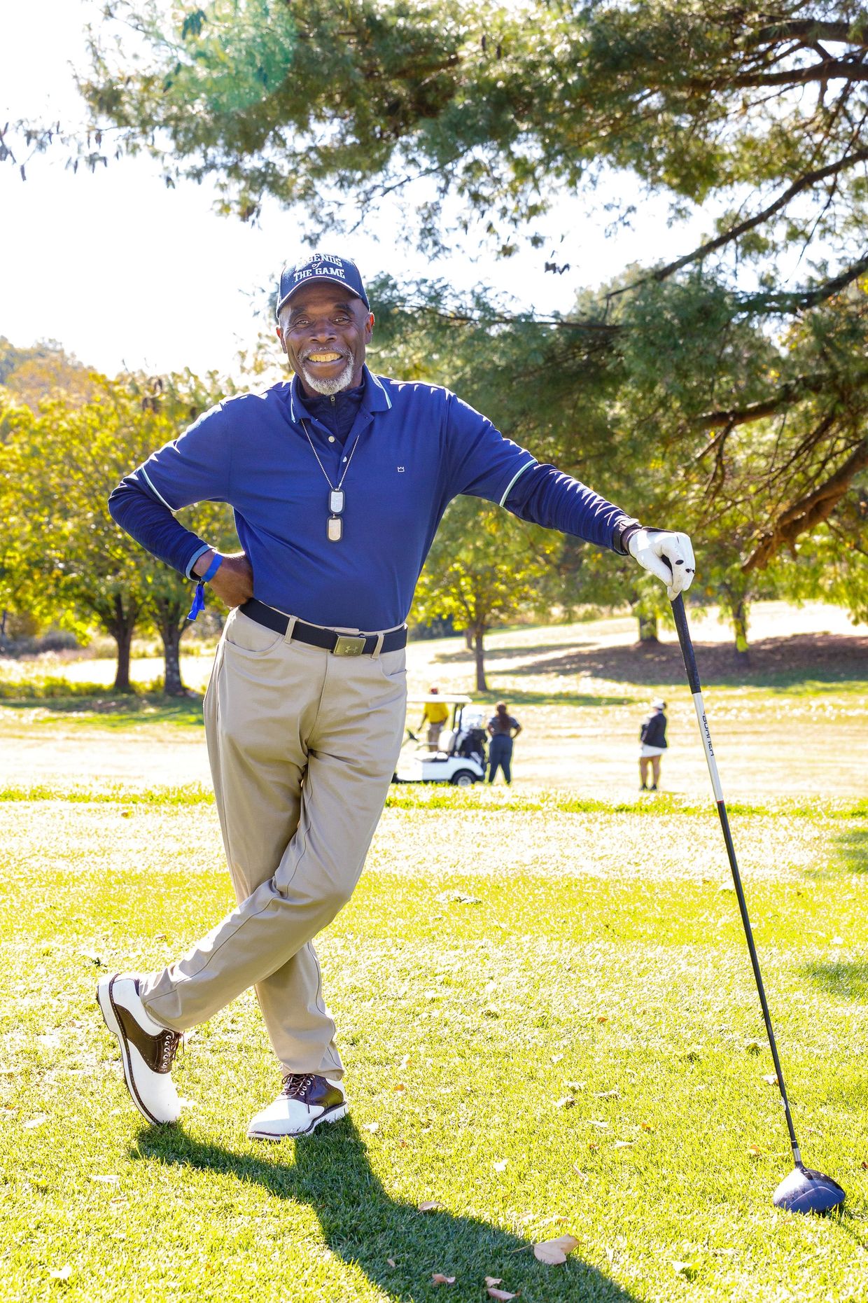 Smiling man posing with a golf club on a sunny golf course.