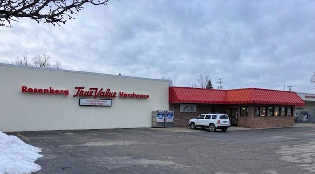 Exterior of Rosenberg True Value Hardware store with a red roof and white SUV parked outside.