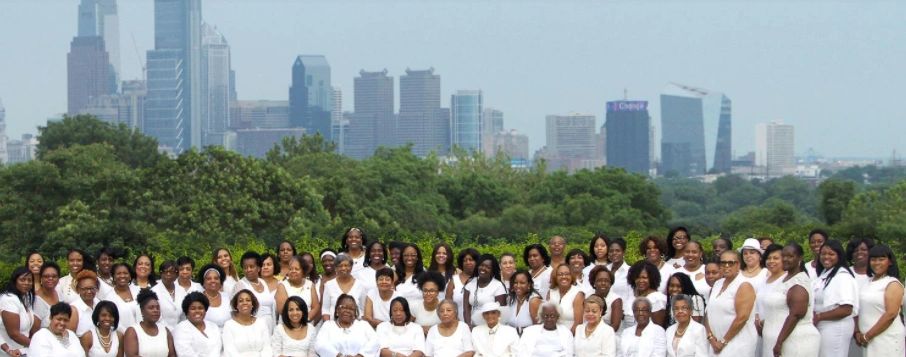 Photo of black women in white in front of the Philadelphia skyline. 
