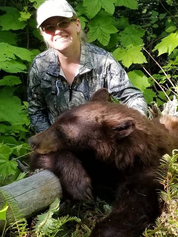 Woman posing with a resting brown bear in a forest.