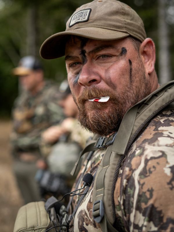 Man with camo face paint and gear looks intensely at the camera.