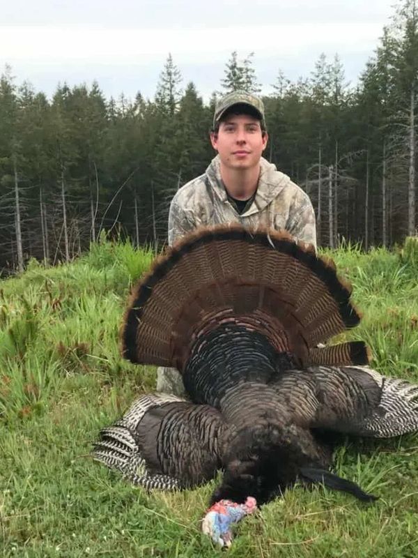 Hunter posing with a wild turkey in a forest clearing.