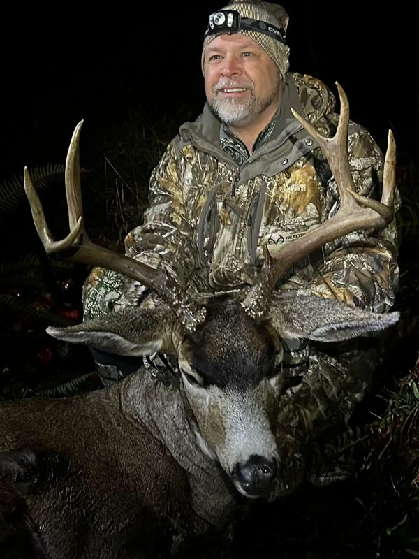 Hunter proudly posing with a large buck deer at night.
