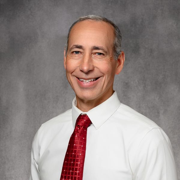 Smiling man in white shirt and red tie against gray background.