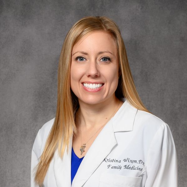 Smiling female doctor in a white coat against a gray background.