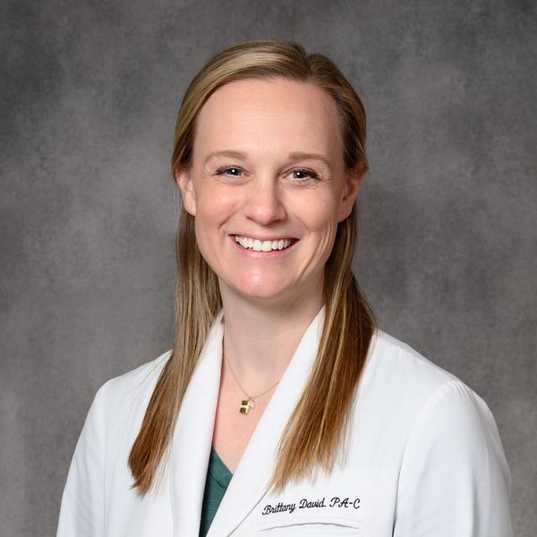Smiling female healthcare professional in white coat against gray background.