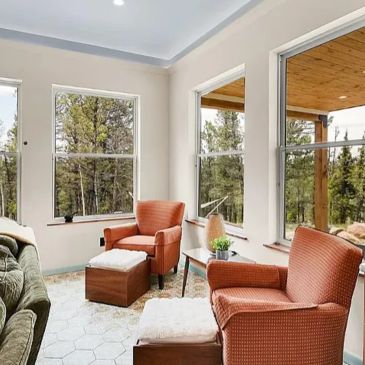Cozy sunroom with orange armchairs and large windows overlooking a forest.