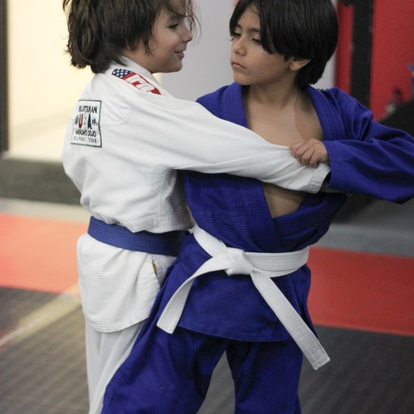Two kids practicing Brazilian Jiu-Jitsu with focused expressions.