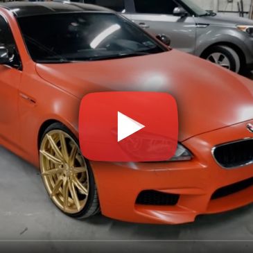 Matte orange BMW with gold rims in a garage.