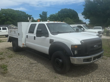 White Ford utility truck parked on gravel under blue sky.