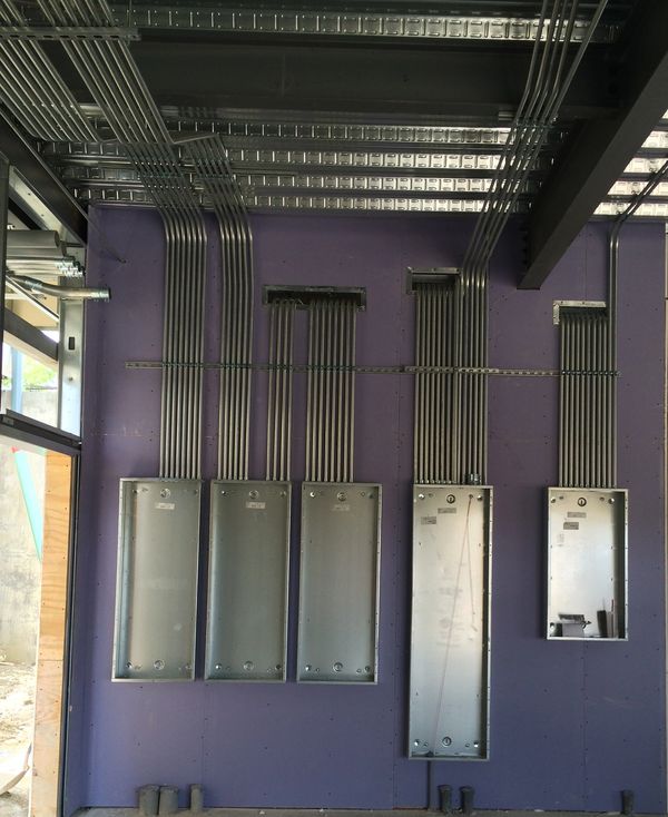 Metal conduit pipes organized neatly on a purple wall in a construction site.