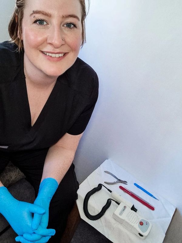 Woman in black scrubs with blue gloves smiling beside medical tools.