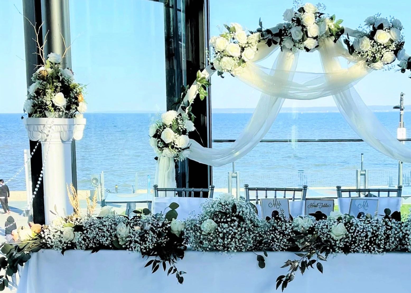 Bridal party head table with baby's breath and white roses and coloums overlooking the lake 