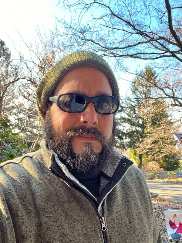Man with a beard wearing sunglasses and a beanie outside.