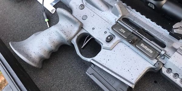 Close-up of a modern rifle with a speckled gray finish.