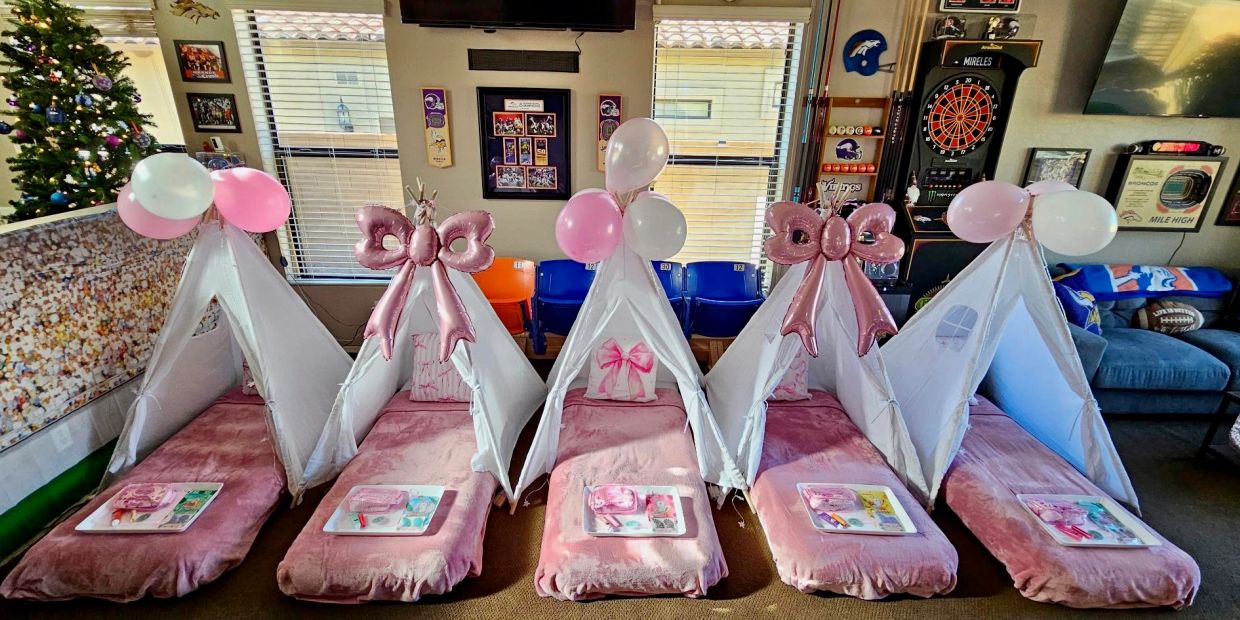 Five pink-themed children's teepees with balloons and mats arranged indoors.