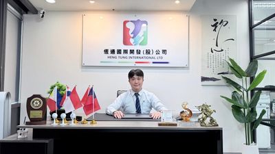 A professional man in a formal office with flags and awards on the desk.