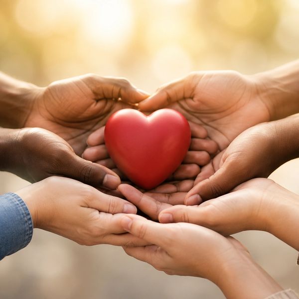Multiple hands holding a red heart together symbolizing unity and care.
