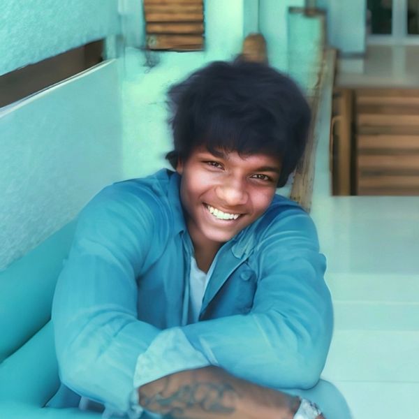 A young man smiling warmly while sitting comfortably indoors.