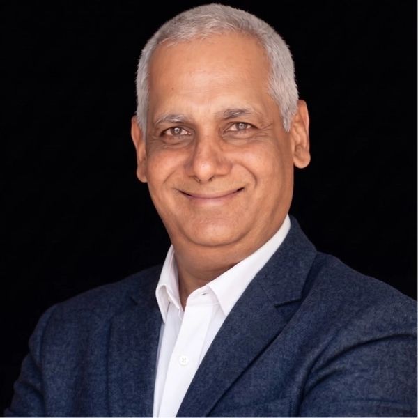 Smiling middle-aged man in a dark blazer and white shirt against a black background.