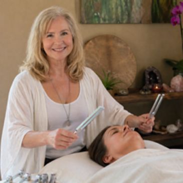A woman performing a sound healing therapy on a client lying down.