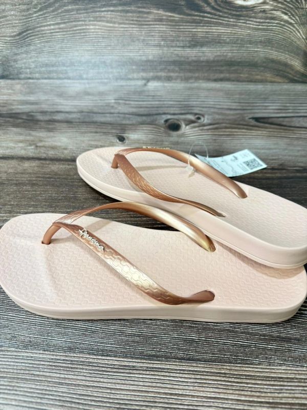 Pair of beige flip-flops with metallic rose gold straps.