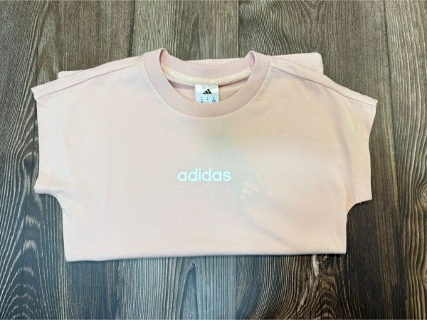 Folded light pink Adidas t-shirt on wooden surface.