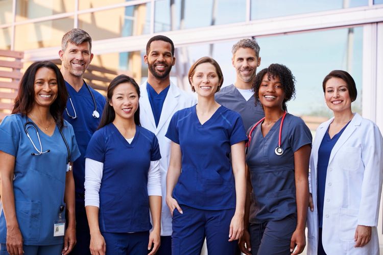Diverse group of healthcare professionals smiling outside a medical facility.