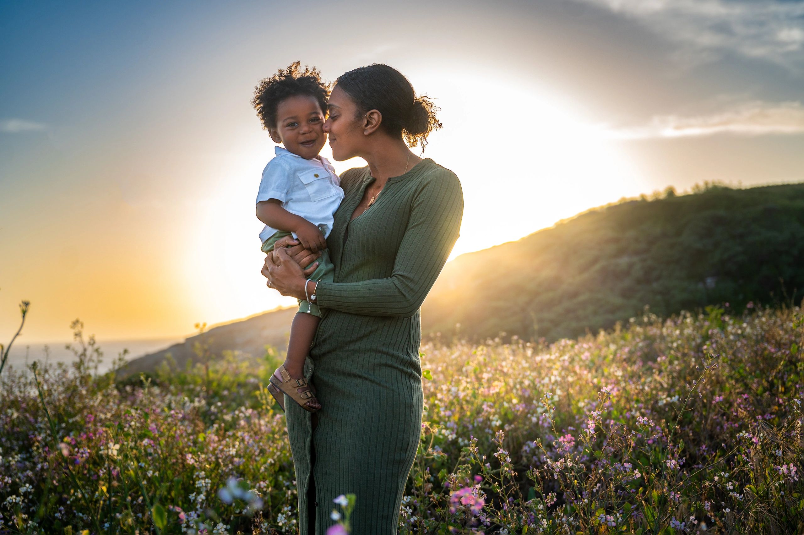 Mother holding child while standing in a field of wildflowers during sunset