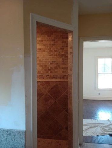 Partially tiled shower with unfinished wall paint and an adjacent room with wooden floor.
