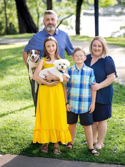 Happy family portrait with two dogs in a sunny park setting.