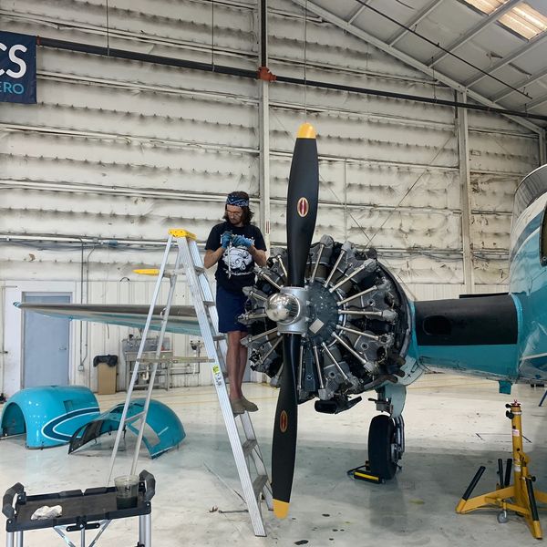 A man works on a vintage airplane engine inside a hangar.