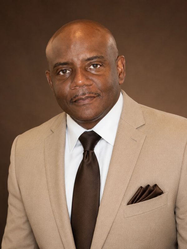 Professional man in beige suit and dark tie against a brown background.