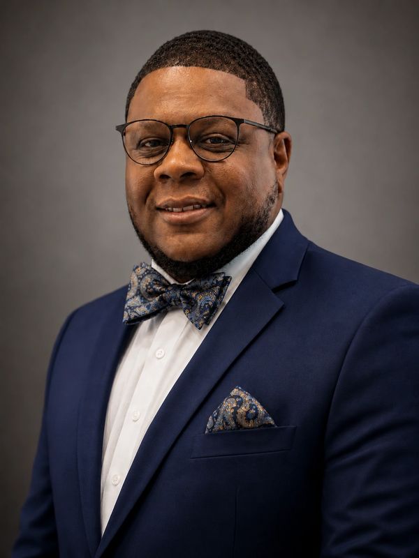 Portrait of a man in a blue suit with bow tie and glasses.
