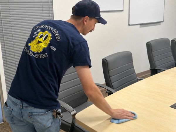 Man cleaning a conference table with a cloth.