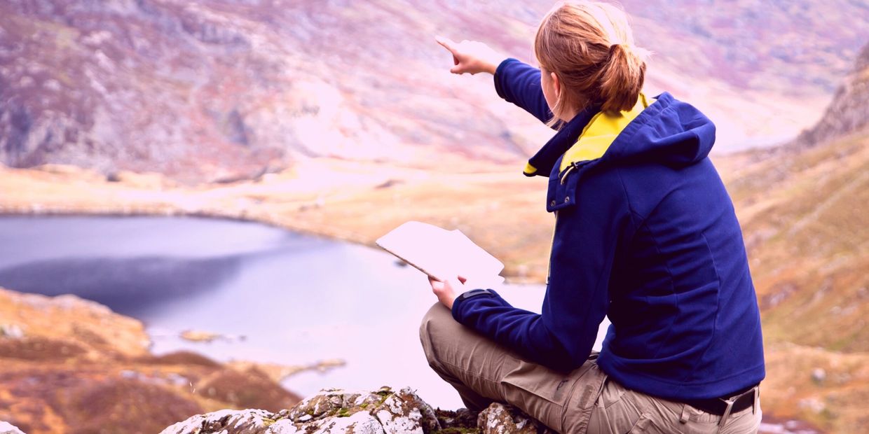 a woman holding a notebook, pointing to the mountain like she knows the way