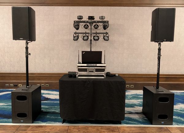 Professional DJ setup with speakers, lighting, and laptop on a black-covered table.