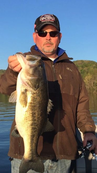 Man holding a large bass fish by a lake.