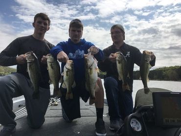 Three men proudly display their impressive bass catches on a boat.