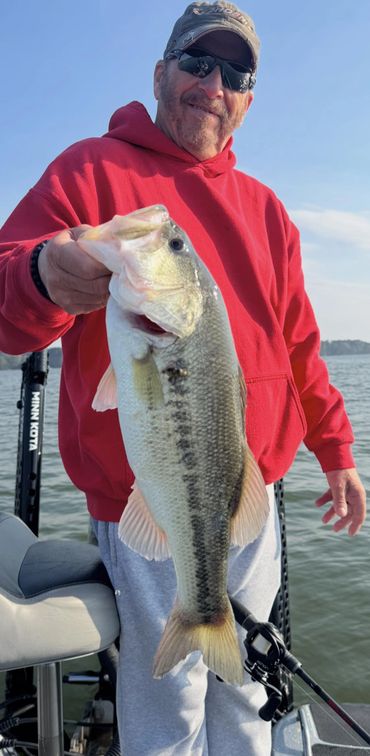 Man in red hoodie proudly holding a large fish on a boat at the lake.
