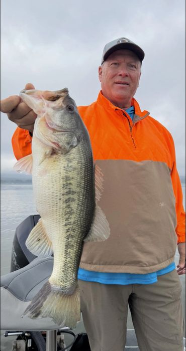Man holding a large fish on a boat, wearing an orange jacket.