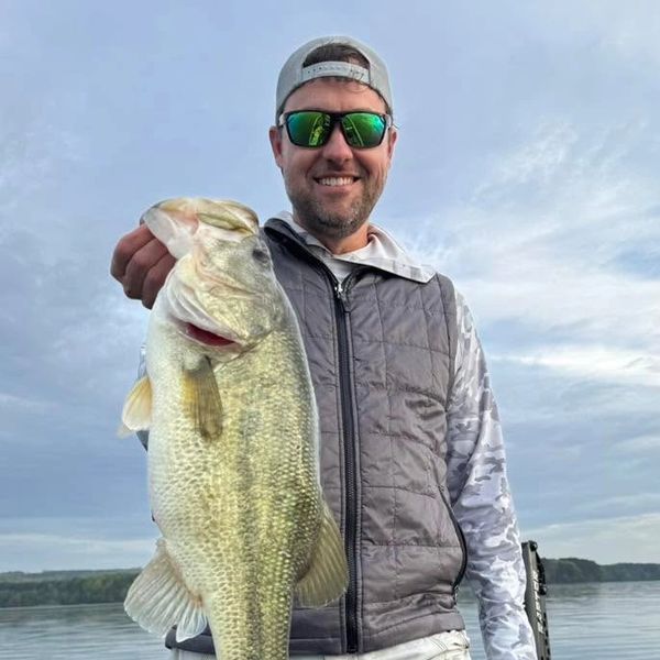 Man holding a large fish with a smile, wearing sunglasses and a cap.