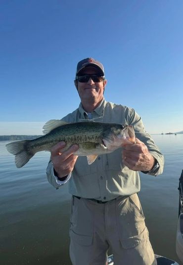 Man holding a largemouth bass on a boat with a lake background.