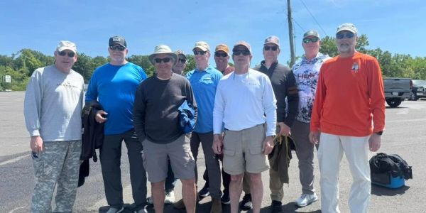 A group of nine men standing outdoors on a sunny day.