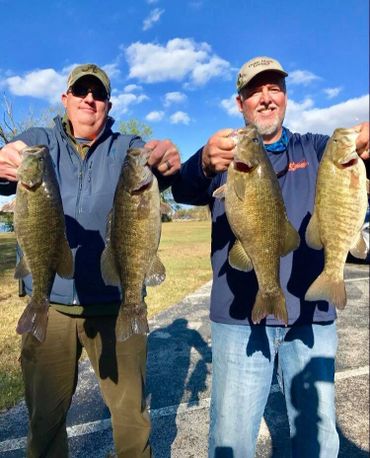 Two men proudly holding four large fish they caught outdoors.