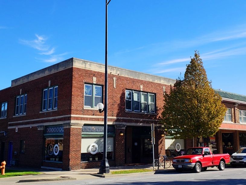 Brick building on a sunny street corner with parked cars and a tree.