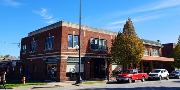 Brick building on a sunny street corner with parked cars and a tree.