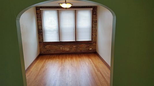 Empty room with wooden floor, brick wall, and three windows with blinds.