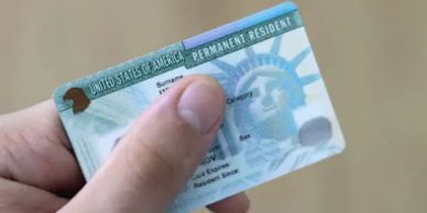 Hand holding a U.S. Permanent Resident Card showing part of the Statue of Liberty.